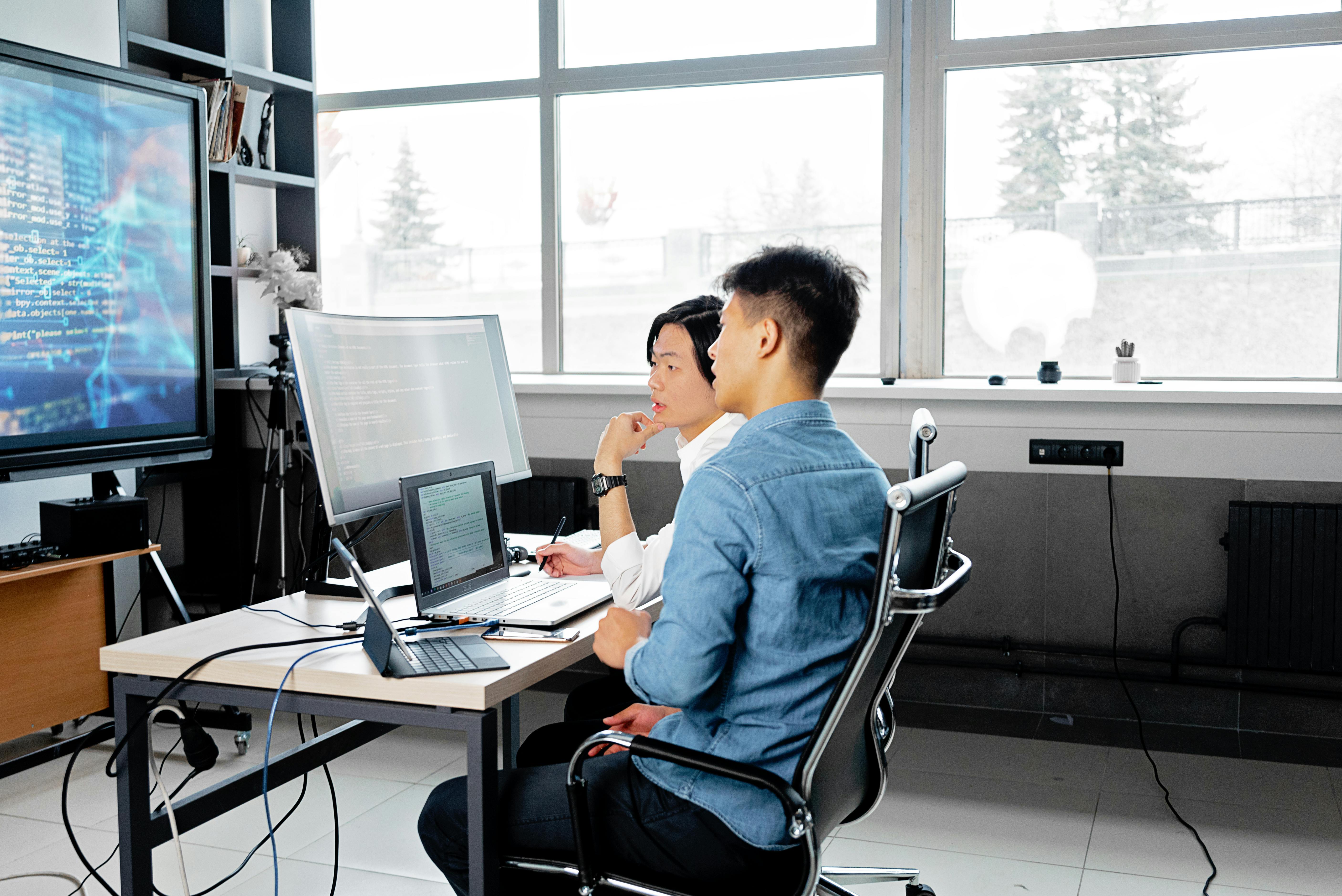 Two men analyzing code on computers in a modern office setting.