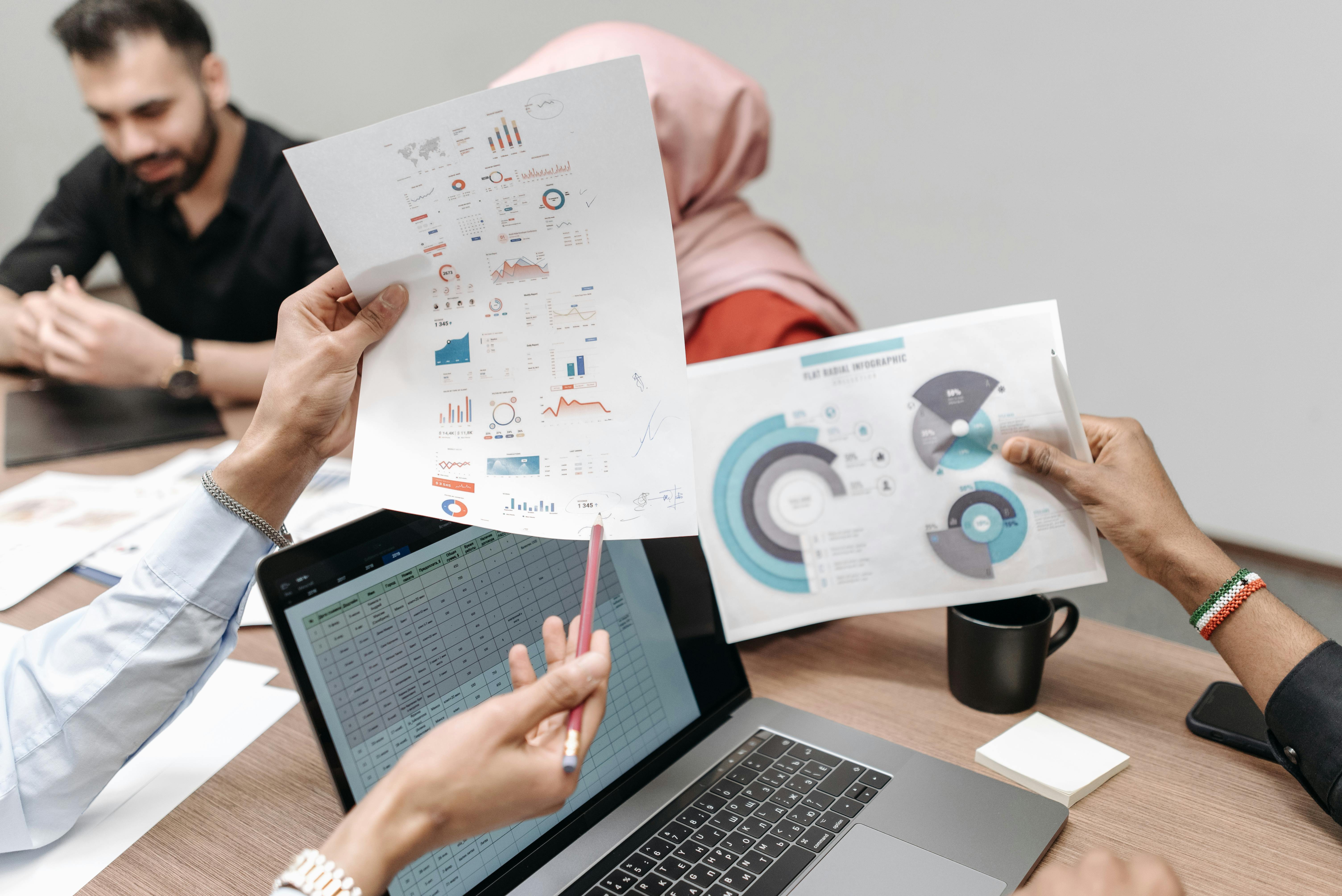 Team analyzing graphs and data during a business meeting, showcasing hands-on engagement with paperwork and laptops.
