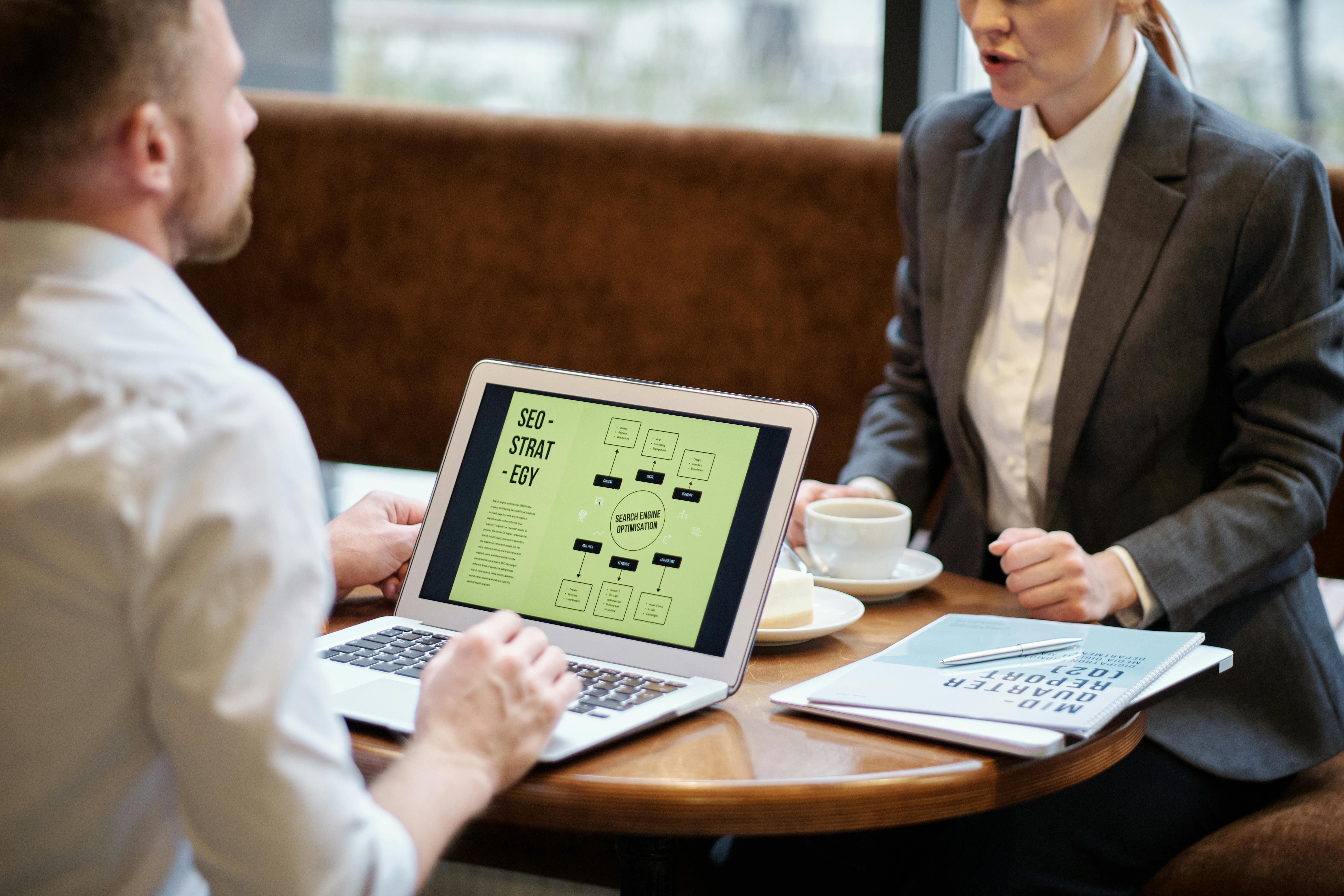 A man and woman engaged in a business meeting discussing SEO strategy in a cozy cafe setting.