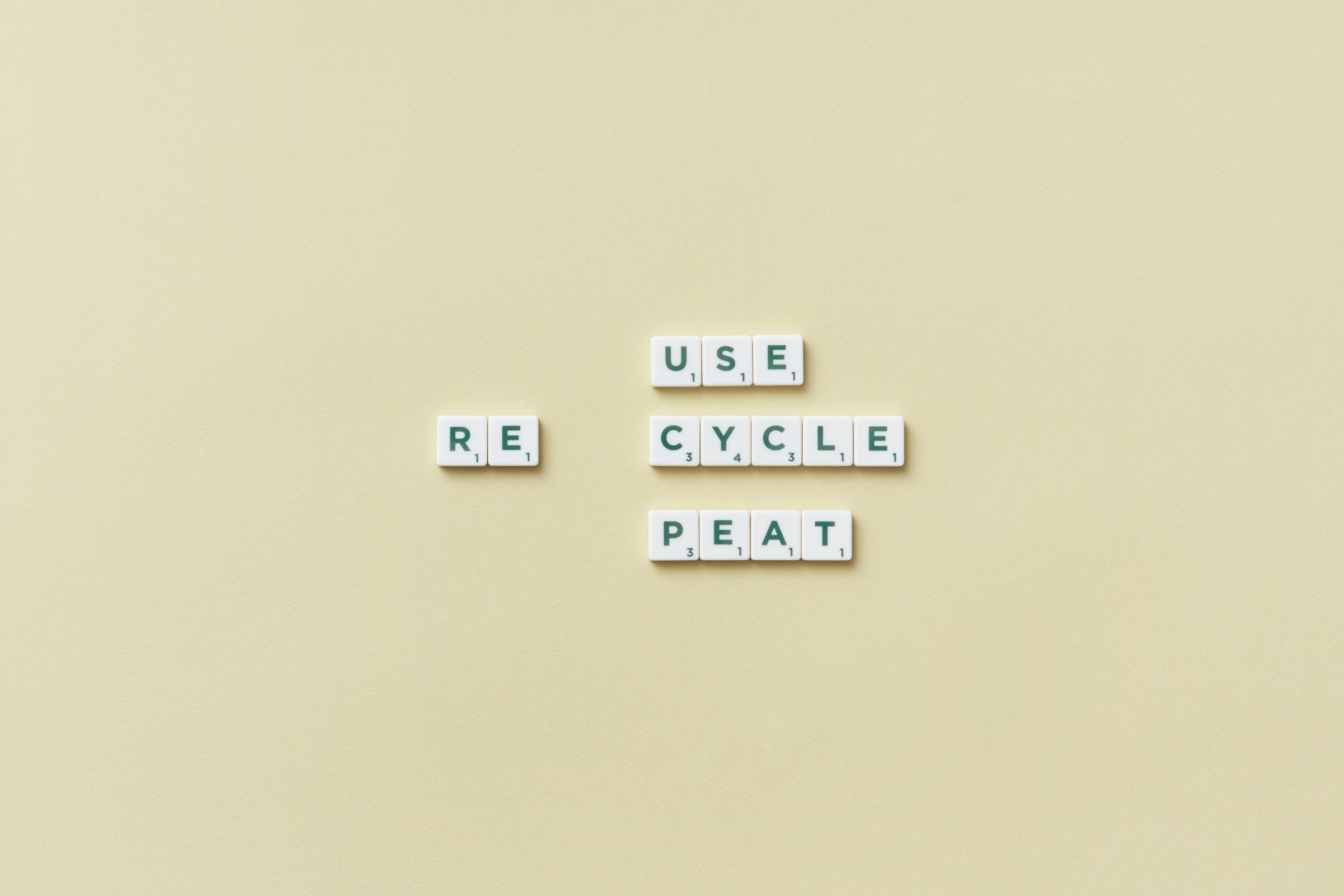 Letter tiles spelling 'reuse recycle repeat' on a simple background, promoting sustainability.