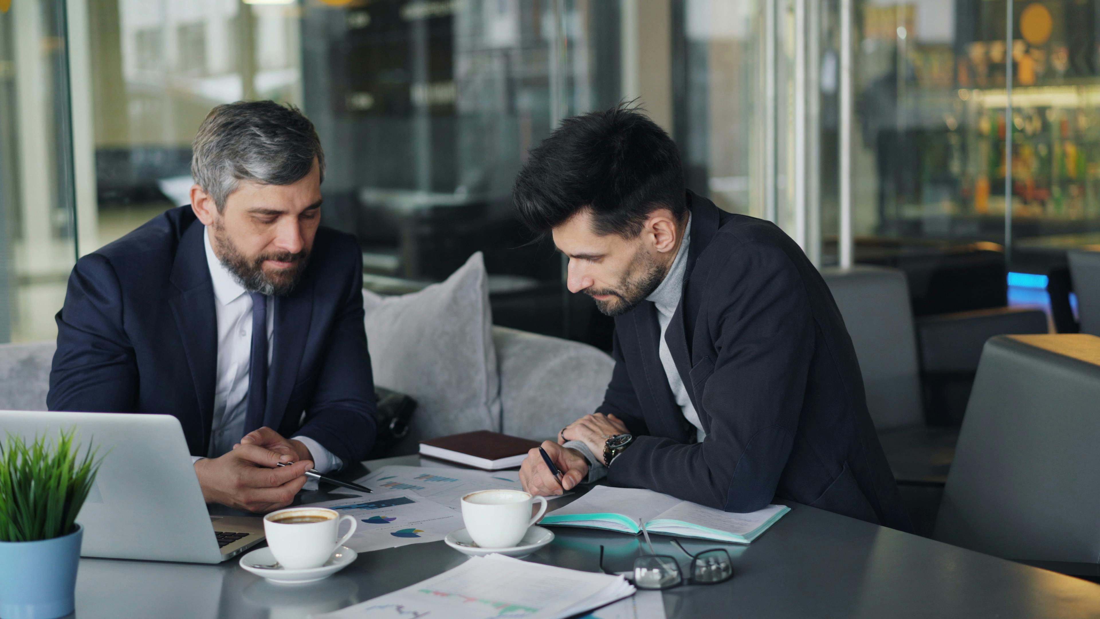 Two businessmen discussing charts over coffee at a café.